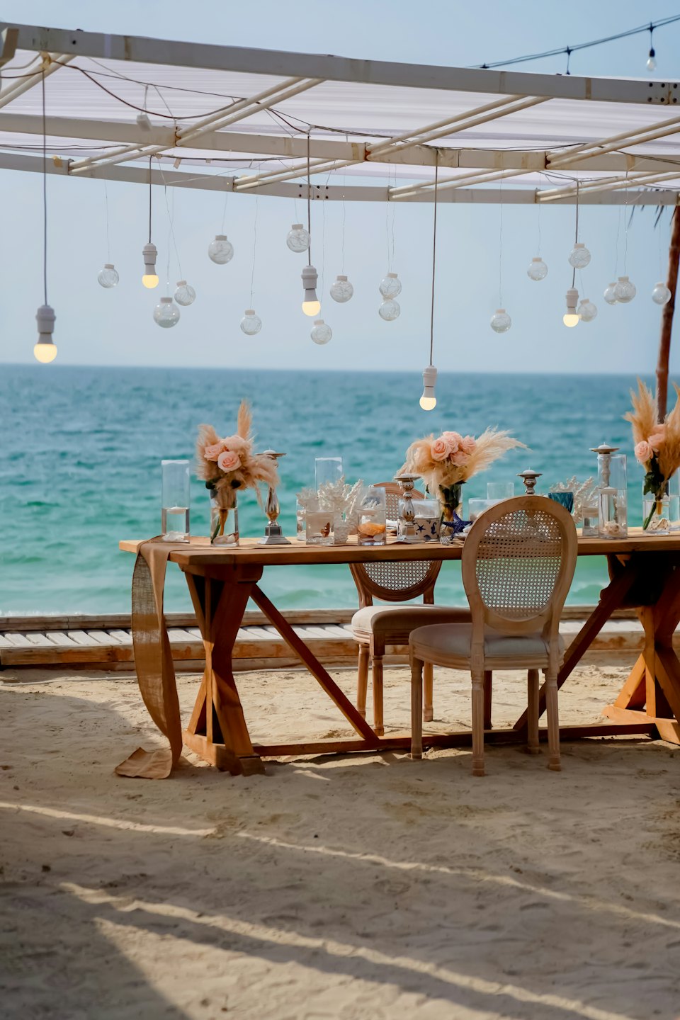 Tavola da pranzo apparecchiata per un evento in spiaggia sotto una tettoia.