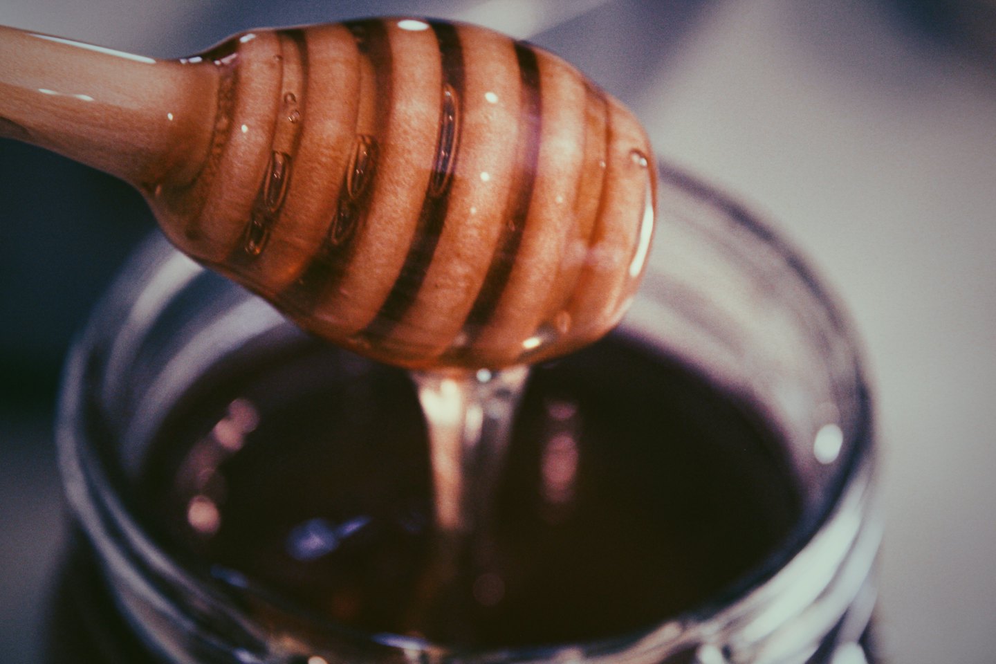 Miele dorato cola da un mestolo di legno in un barattolo.